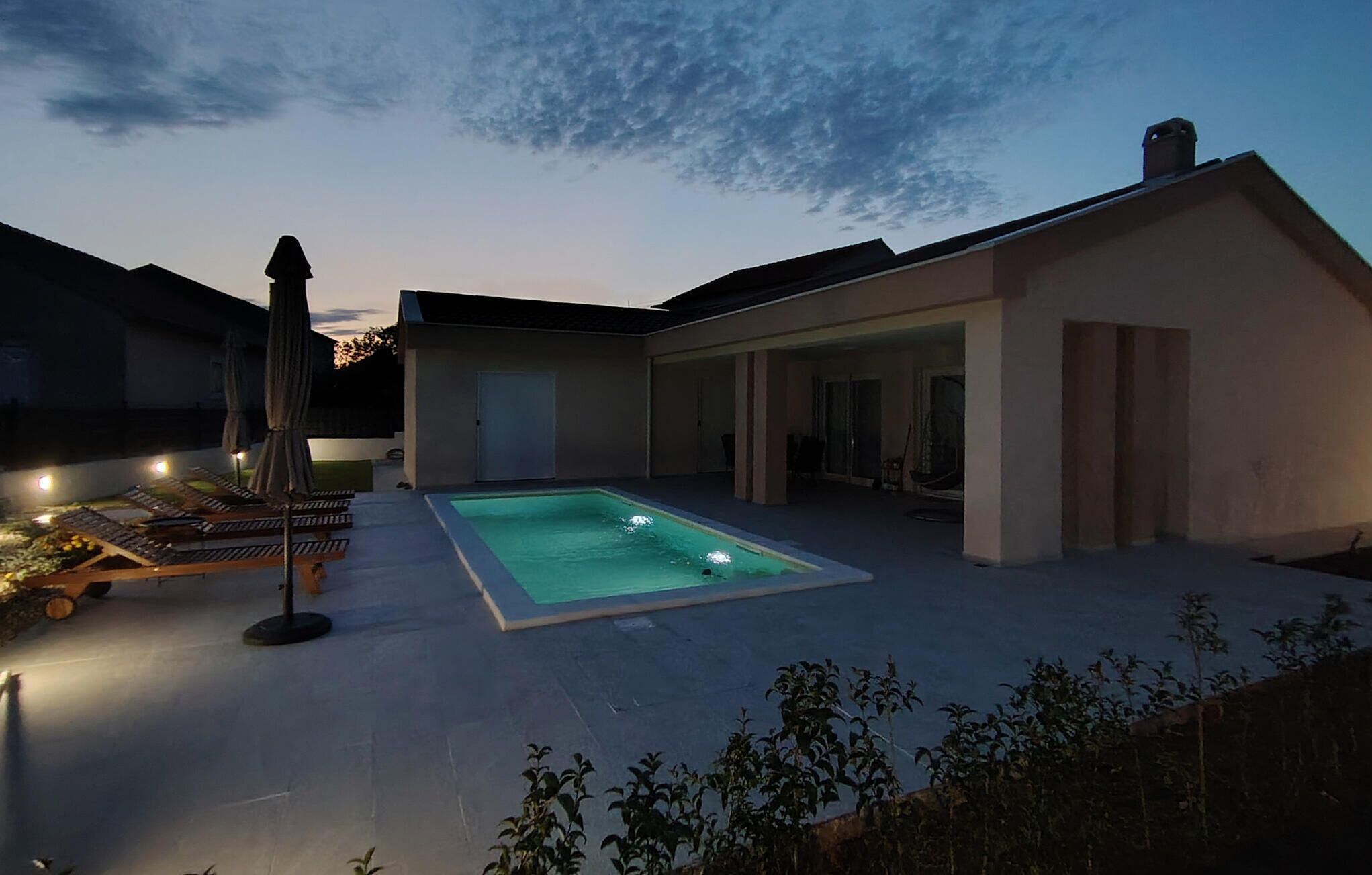 Ett modernt hus med en swimmingpool, en täckt uteplats och ett väl upplyst utomhusområde.