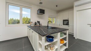 A modern kitchen with a central island, white cabinetry, and a view of trees through large windows. - Luxurious home in Kakma (Kakma)