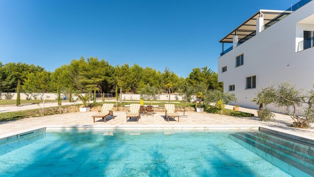 A swimming pool with lounge chairs and a white building in the background. - Luxurious home in Kakma (Kakma)