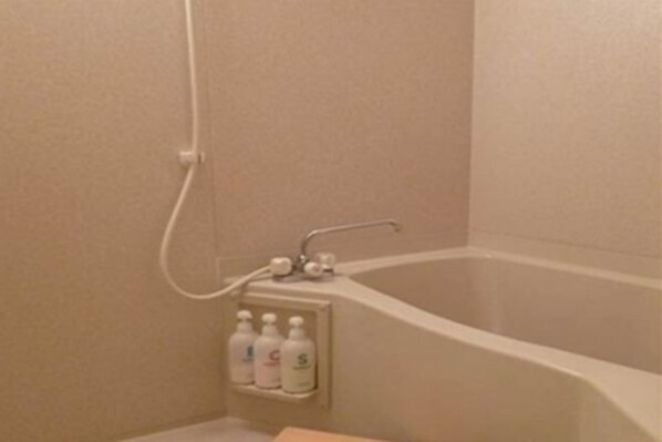 Een badkamer met een bad, een douche en een plank met daarboven drie flessen.