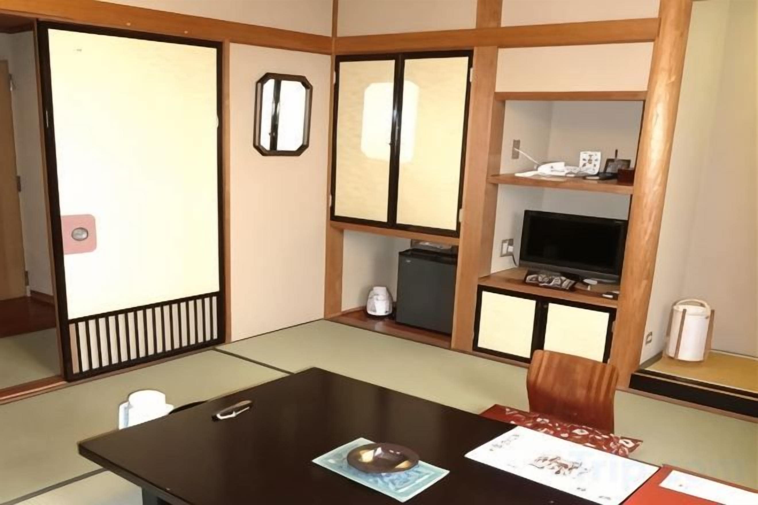 A traditional Japanese room with tatami flooring, a low table, a television, and a shelf with various items.