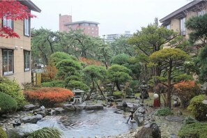 Un jardin japonais traditionnel avec un étang, des rochers et divers arbres.