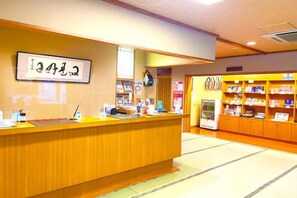 A reception area with a wooden counter, a sign with Japanese characters, and a shelf with various items. - Ryokan Ichinomatsu (Hakodate)