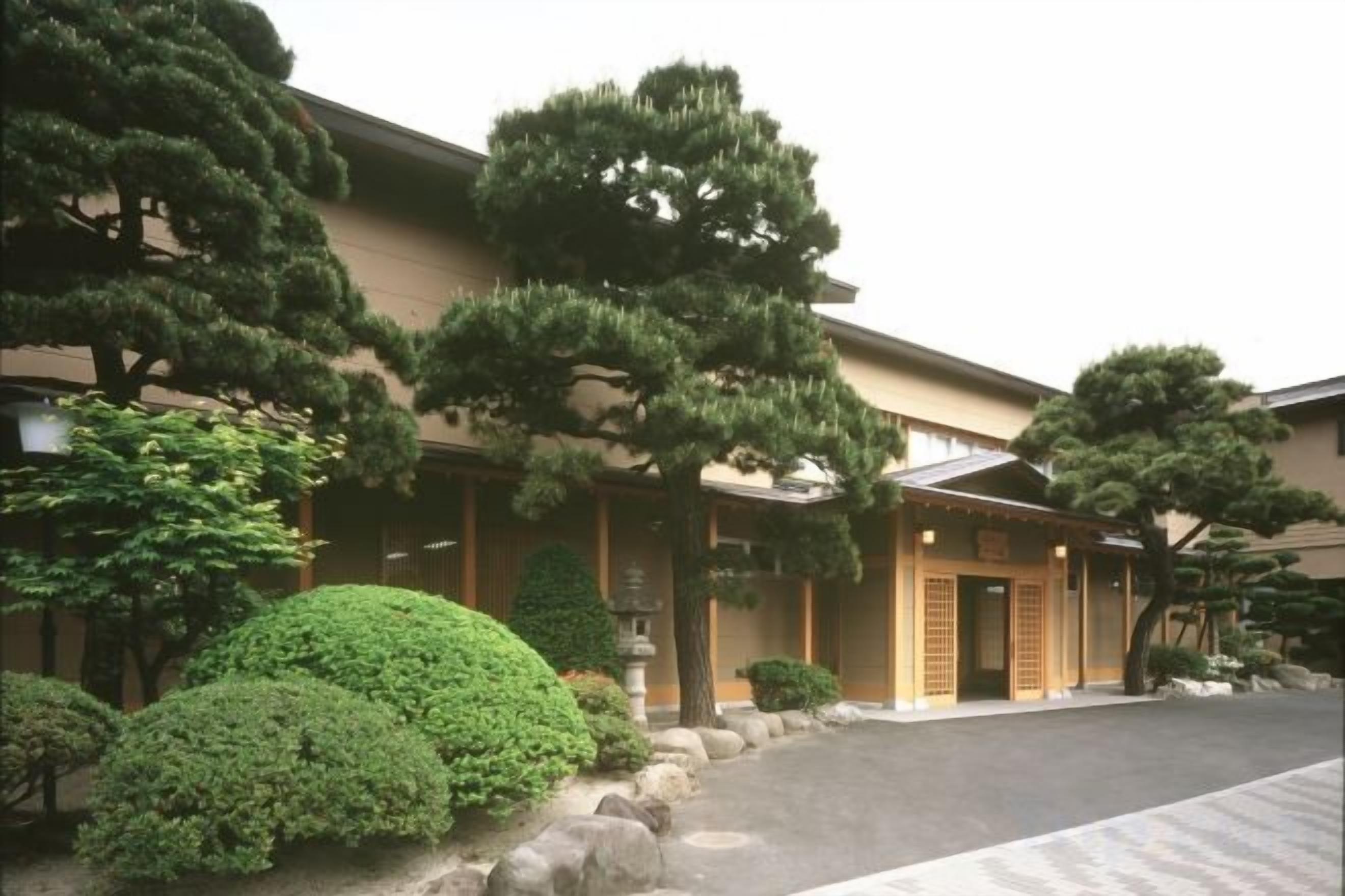 A traditional building with a covered entrance, surrounded by well-maintained trees and shrubs.