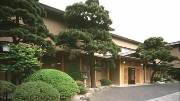A traditional building with a covered entrance, surrounded by well-maintained trees and shrubs.