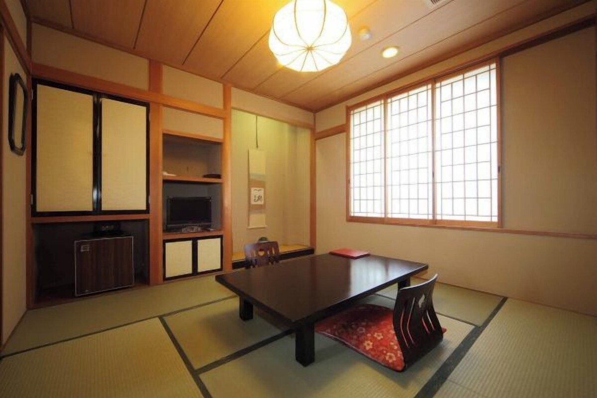 A traditional Japanese room with tatami flooring, a low table, sliding doors, and a large window.