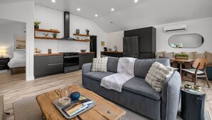 Un espacio habitable moderno con un sofá gris, una mesa de centro de madera y una cocina con armarios negros y una estufa.