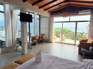 Una habitación con cama, televisión, balcón con vista al mar y zona de comedor.