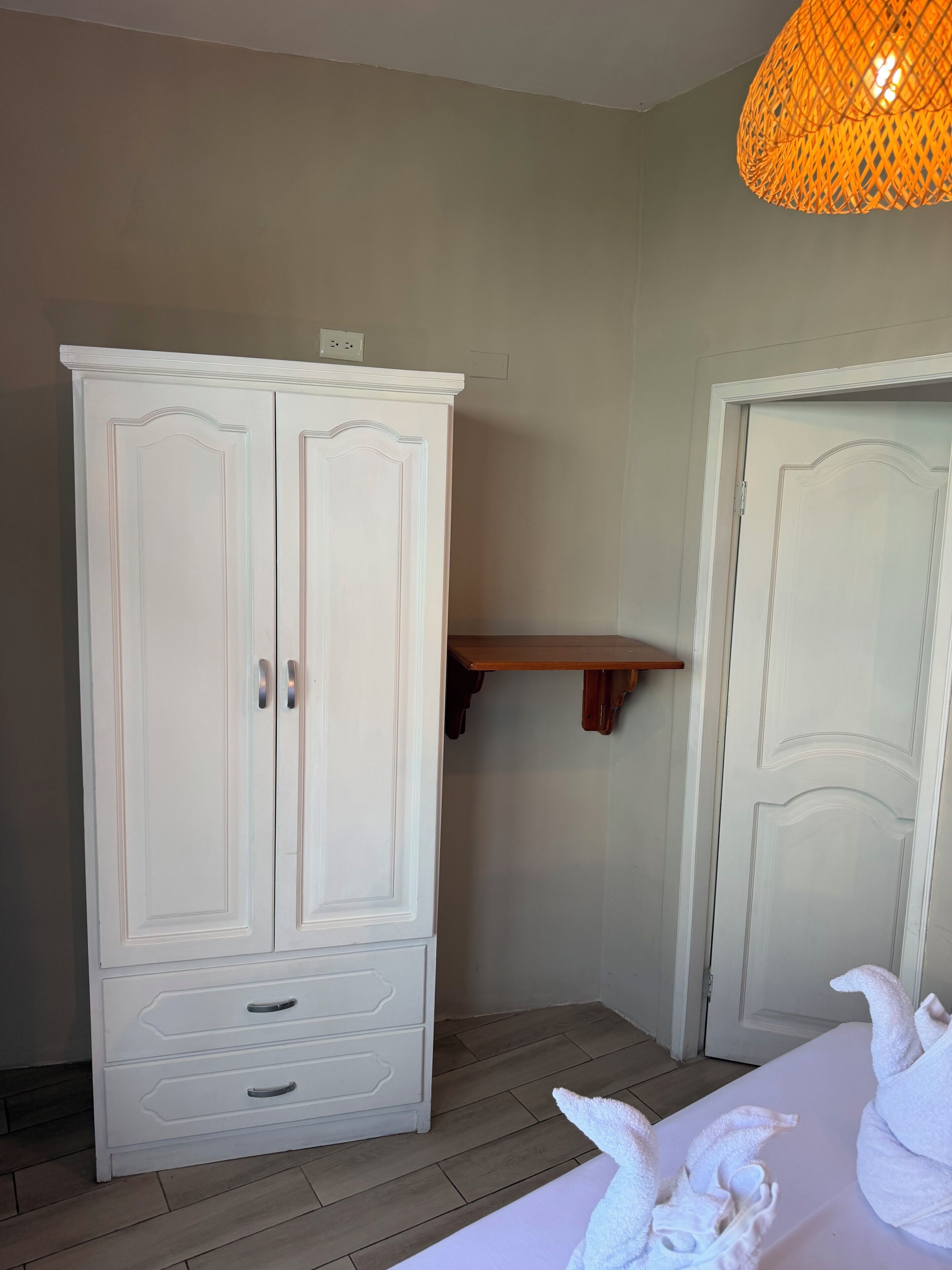 A white wardrobe with two doors and a shelf, a white door, and a hanging light fixture.