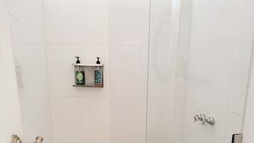 Une douche avec une porte en verre, un porte-serviettes et une étagère pour les articles de toilette.