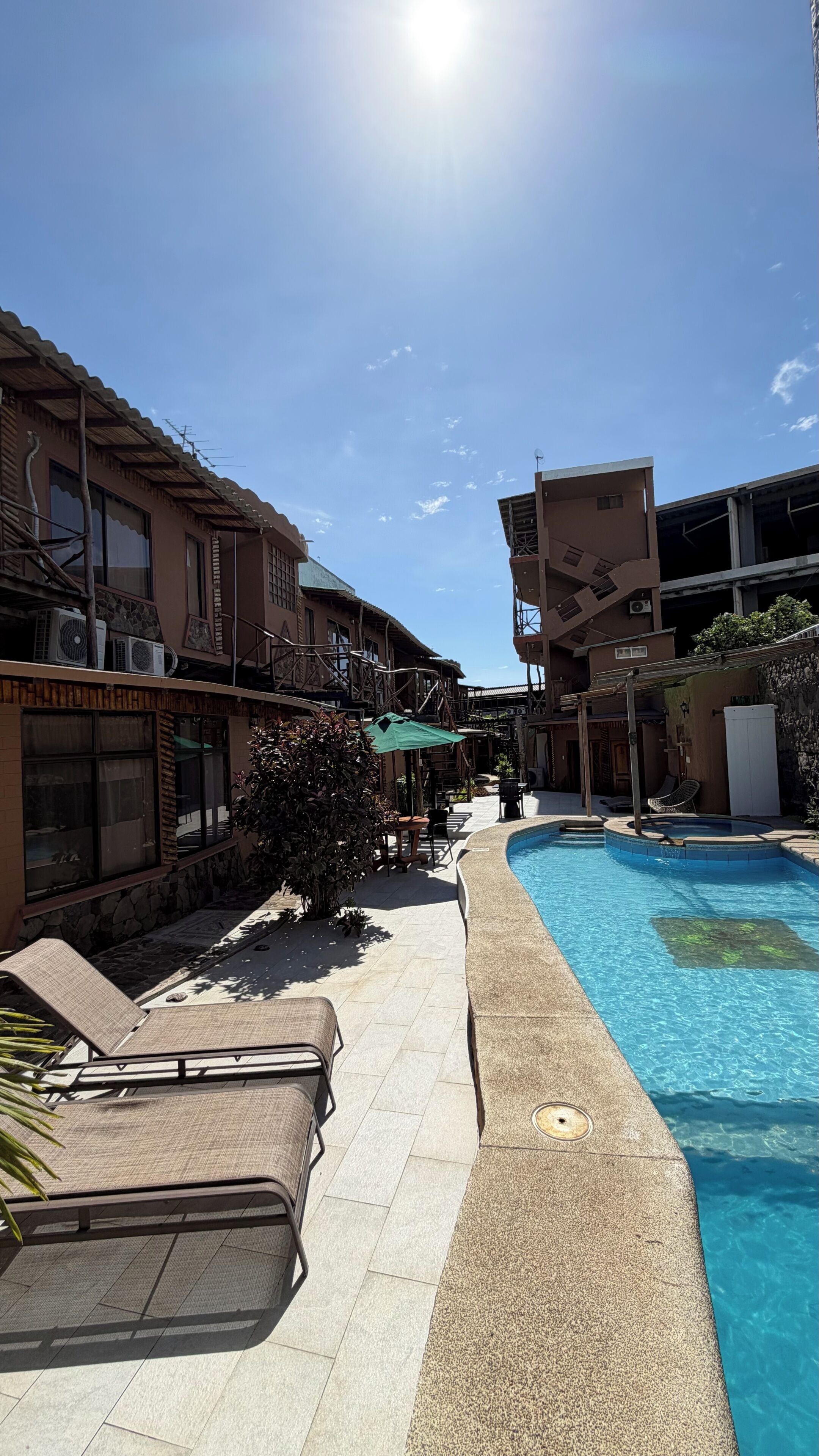 A swimming pool with lounge chairs, a stone pathway, and buildings with balconies and air conditioning units.