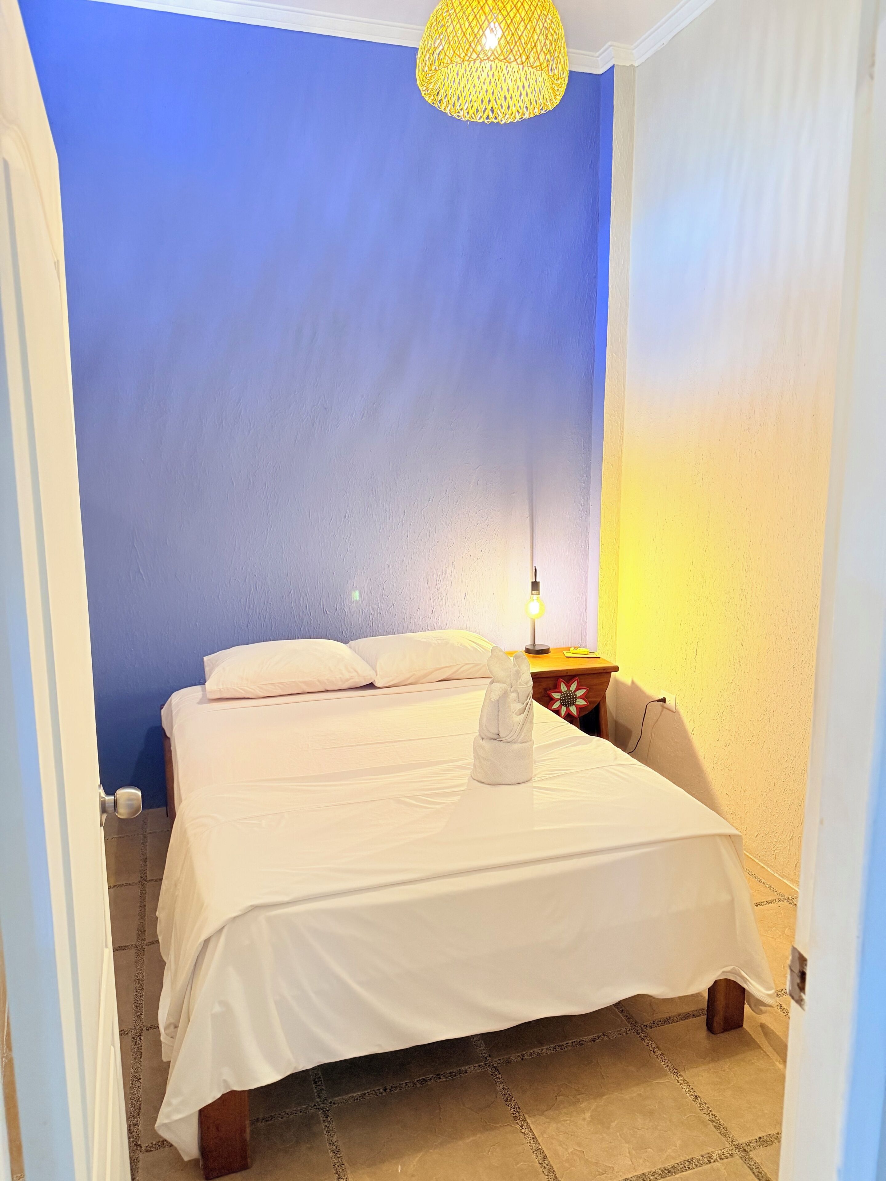 A bedroom with a bed, a nightstand with a lamp, and a wall with a blue and white color scheme.