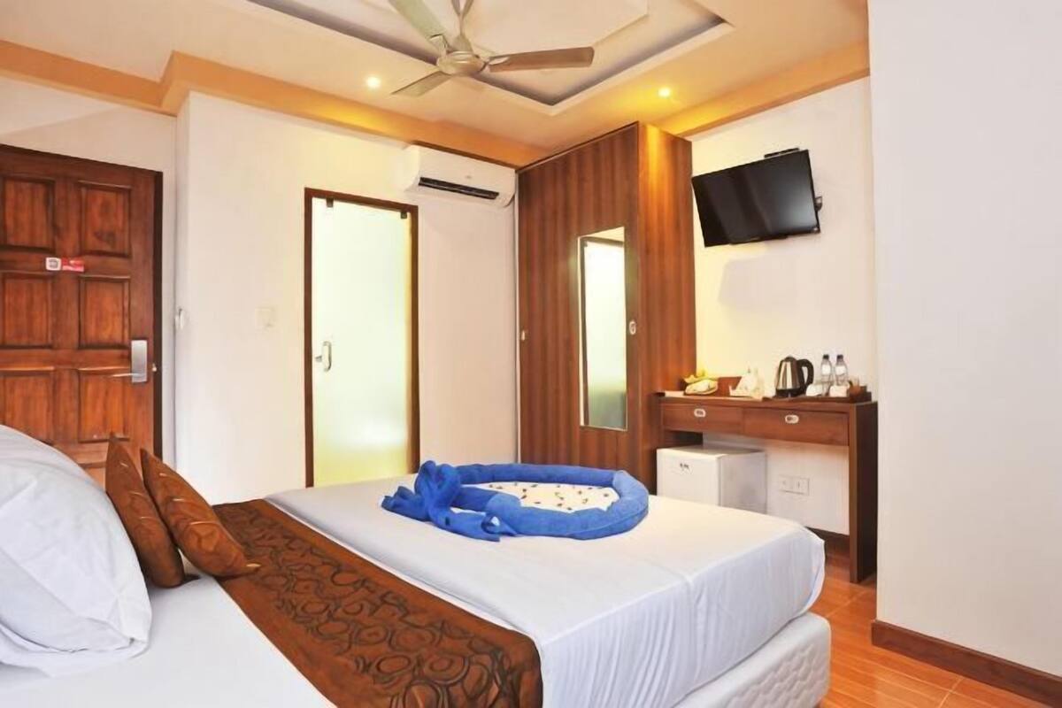 A hotel room with a bed, a desk, a television, and a ceiling fan.