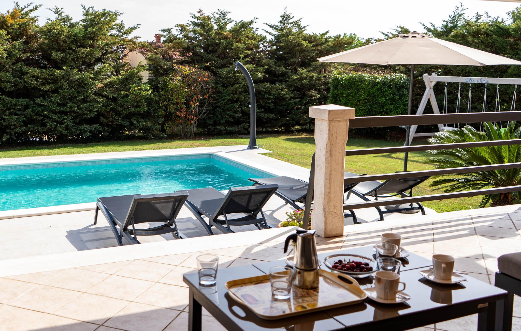 A poolside area with lounge chairs, a table with a tray of drinks, and a view of a swimming pool.