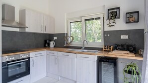 Une cuisine moderne avec des armoires blanches, un four encastré, un lave-vaisselle et une fenêtre donnant sur les arbres.