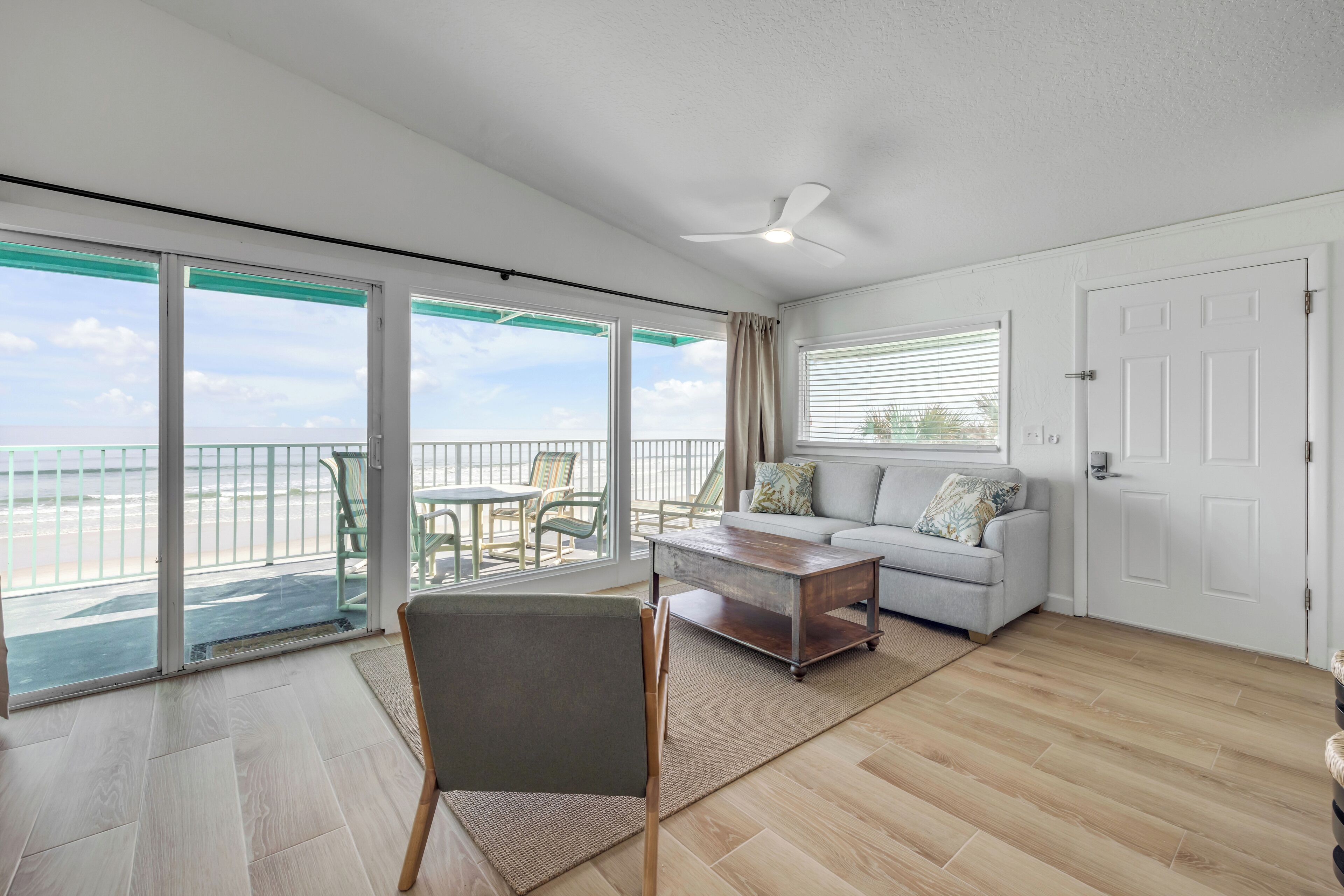 A spacious room with a balcony, a sofa, a coffee table, and a chair.