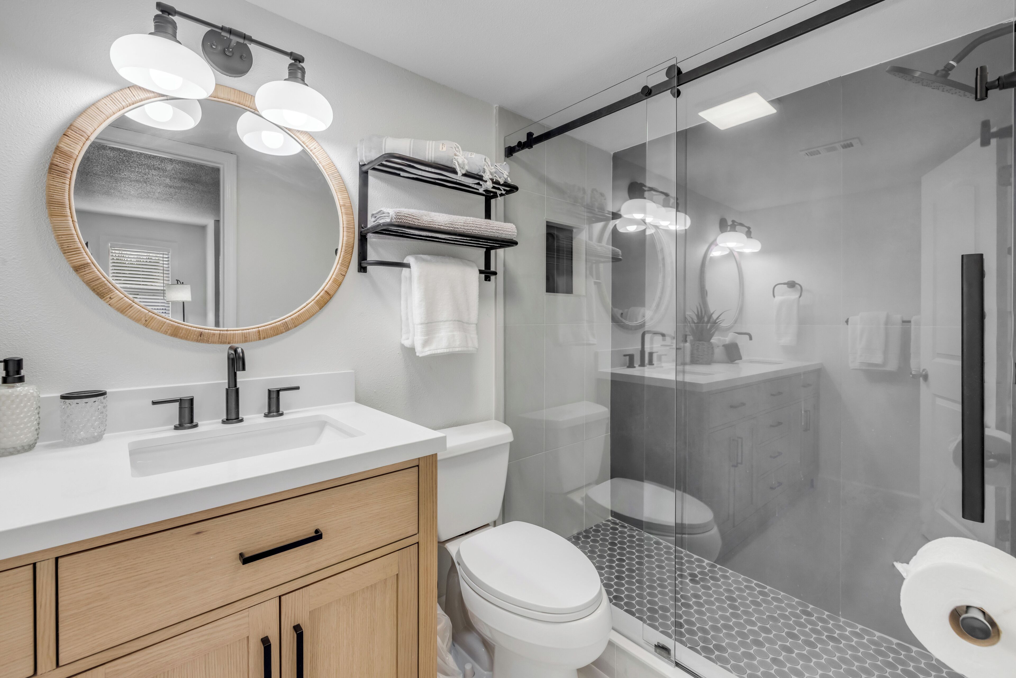 A modern bathroom with a round mirror, dual sinks, a toilet, and a glass-enclosed shower area.