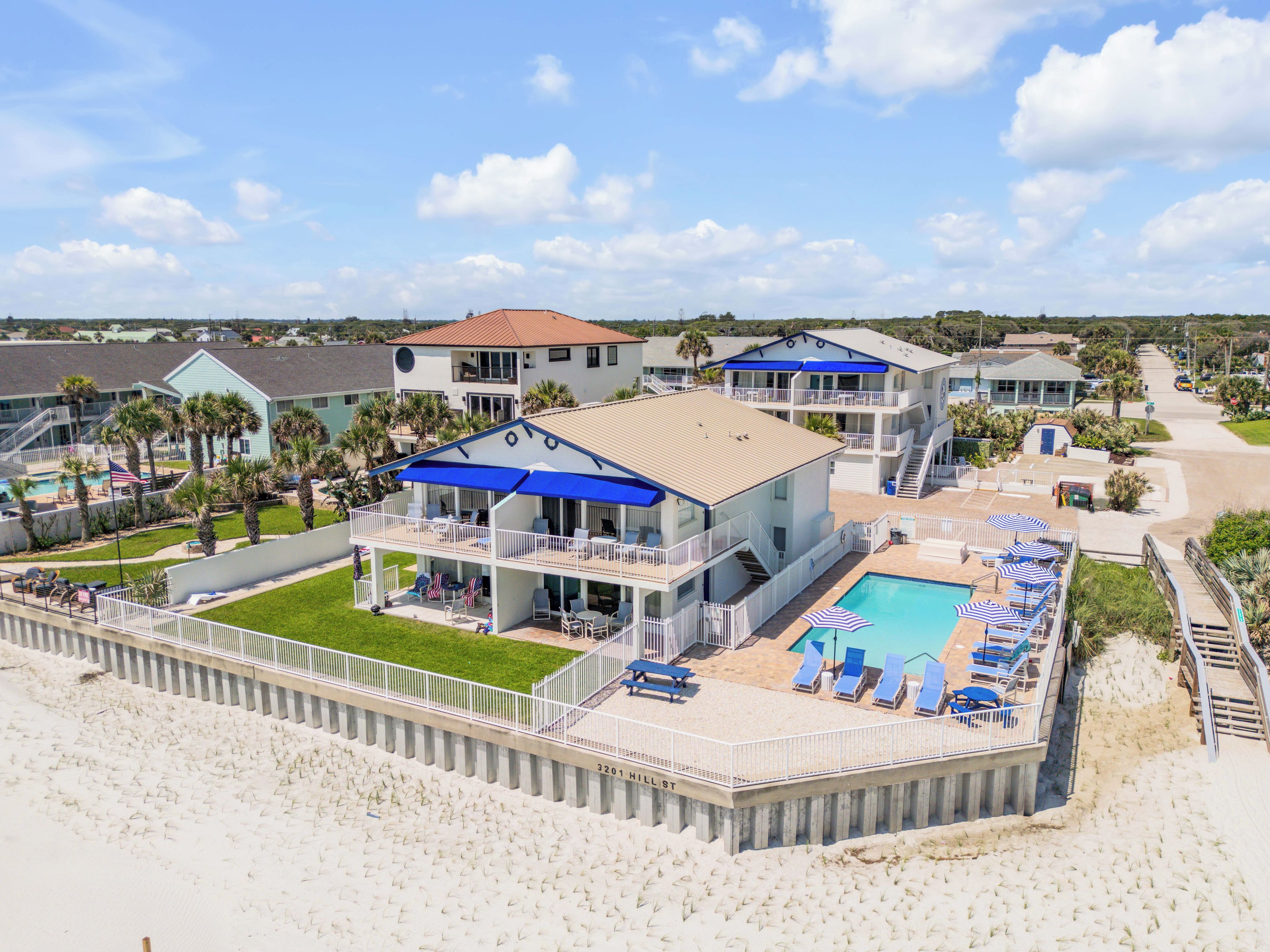 A beachfront property with a pool, multiple balconies, and a beach area with sun loungers.