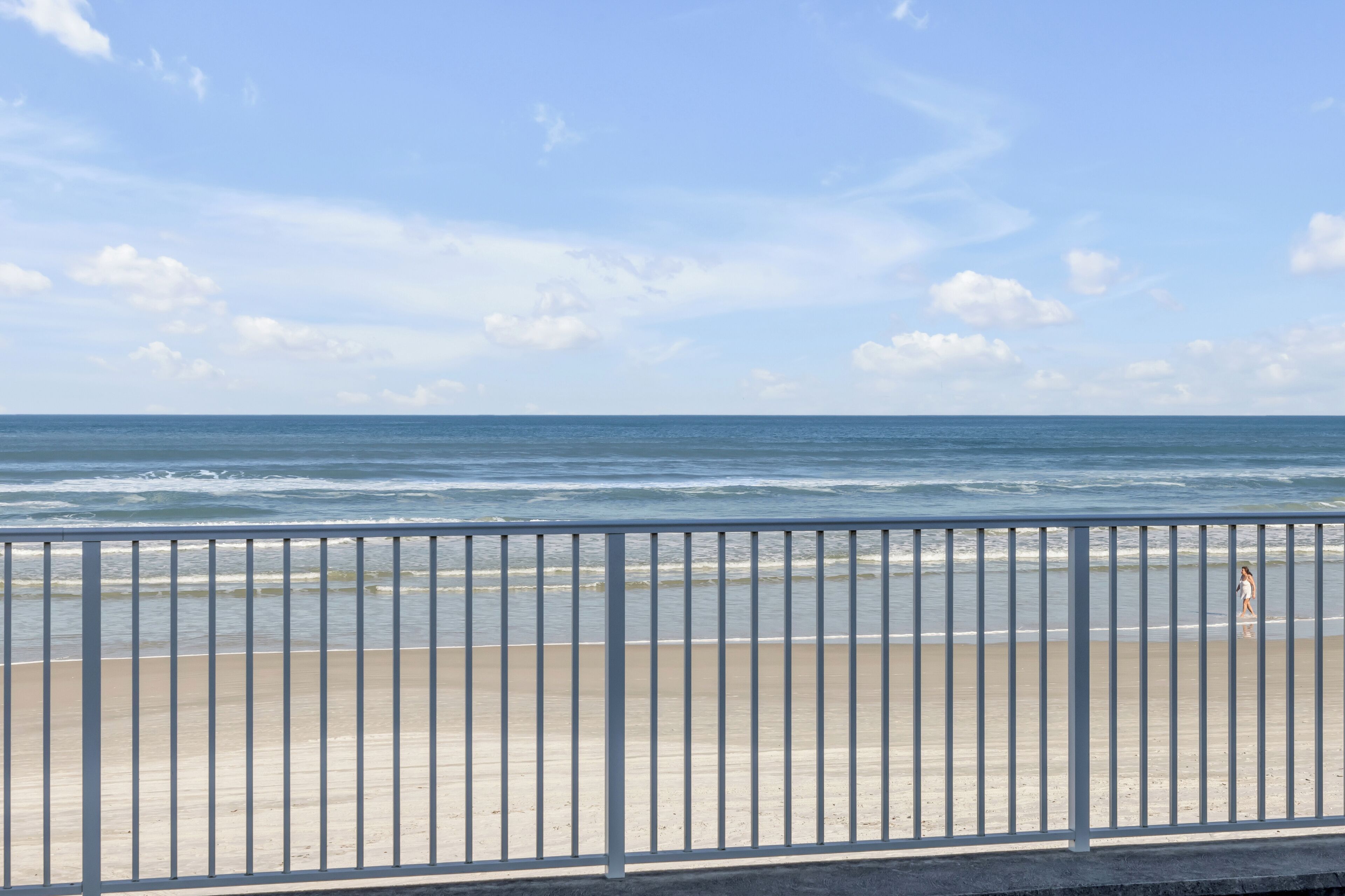 A beach with a metal railing, calm sea, and a clear sky.