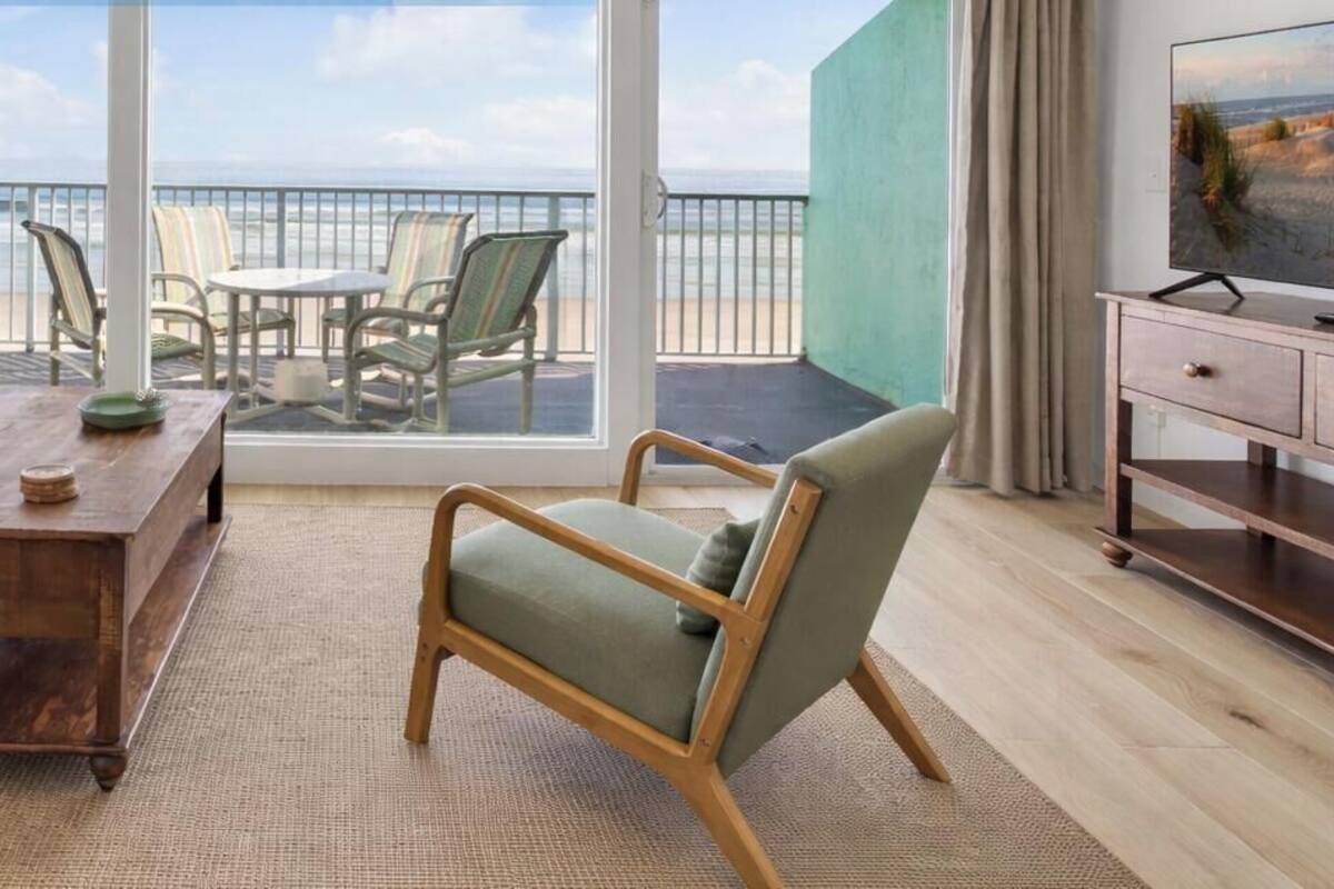Sala de estar com sofá, mesa de centro e poltrona, televisão e varanda com vista para a praia.