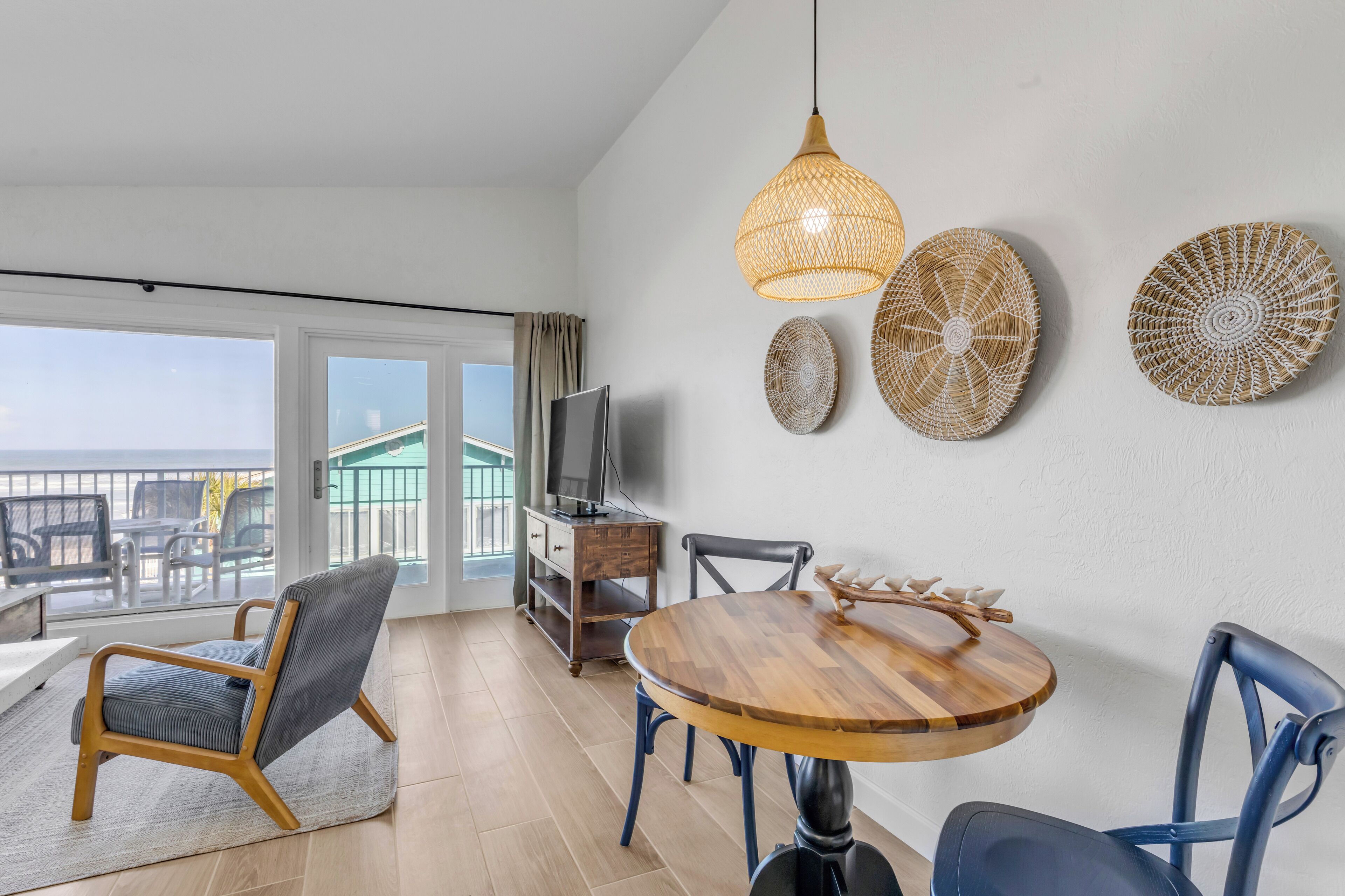 Una sala moderna con una mesa de comedor de madera, sillas azules, un televisor y un adorno de pared tejido.