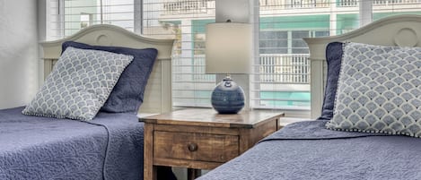 A bedroom with two beds, a nightstand, a lamp, and a window with a view of buildings.
