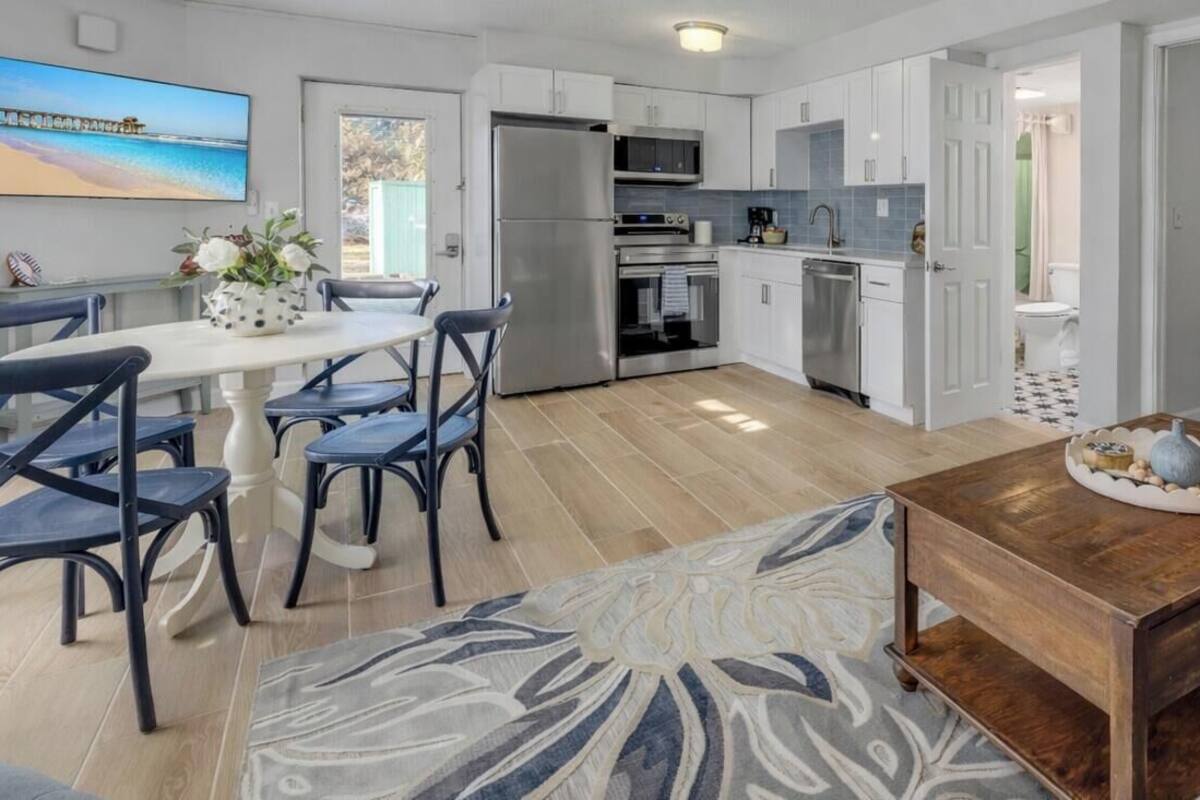Uma cozinha moderna com armários brancos, um espaço de refeições com mesa e cadeiras, e uma sala de estar com sofá e mesa de centro.