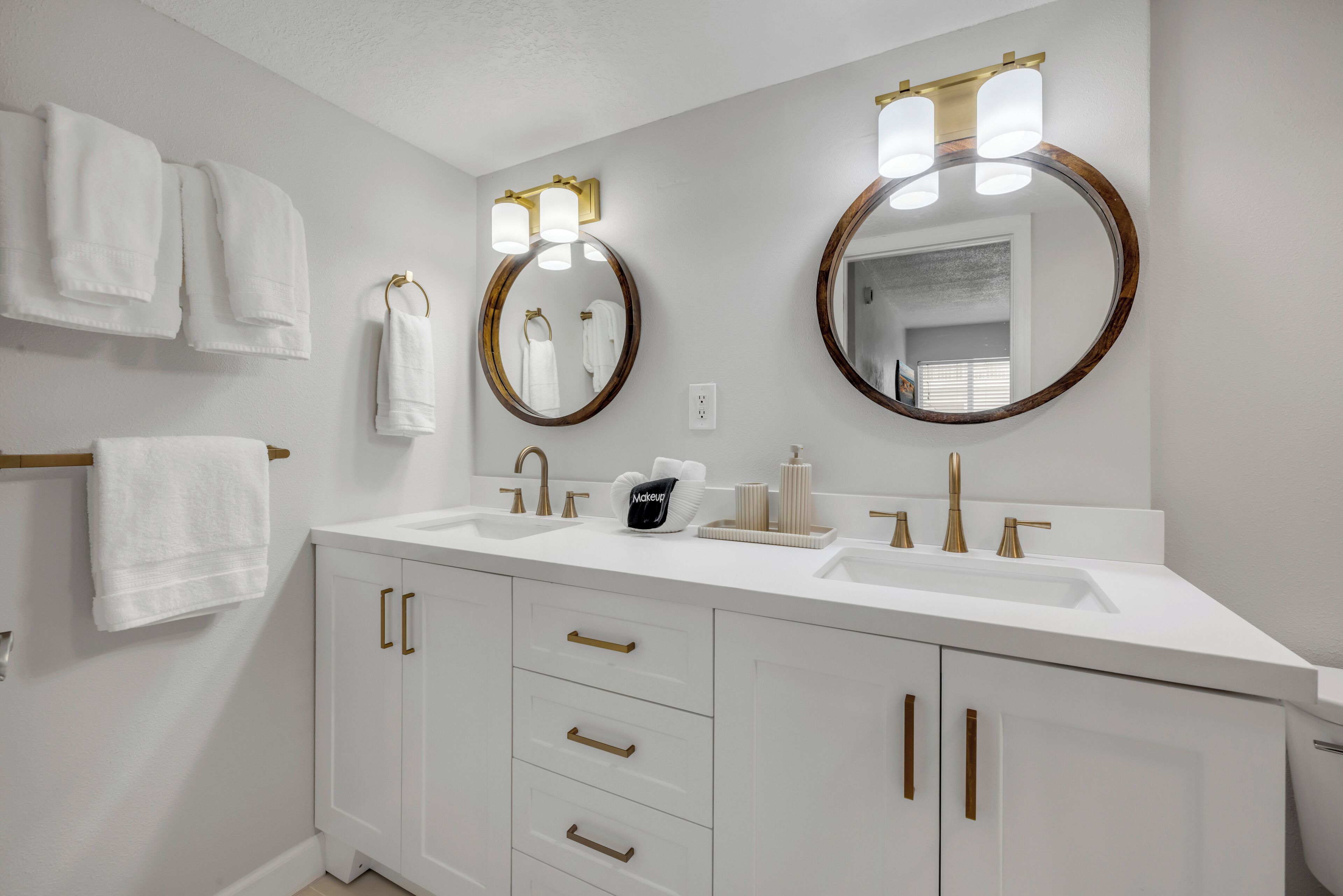 A modern bathroom with two sinks, gold handles, a large mirror, and white towels.