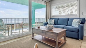 A living room with a blue sofa, a wooden coffee table, and a view of the balcony.