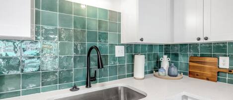 A modern kitchen with a stainless steel sink, white cabinets, and green tiled backsplash.