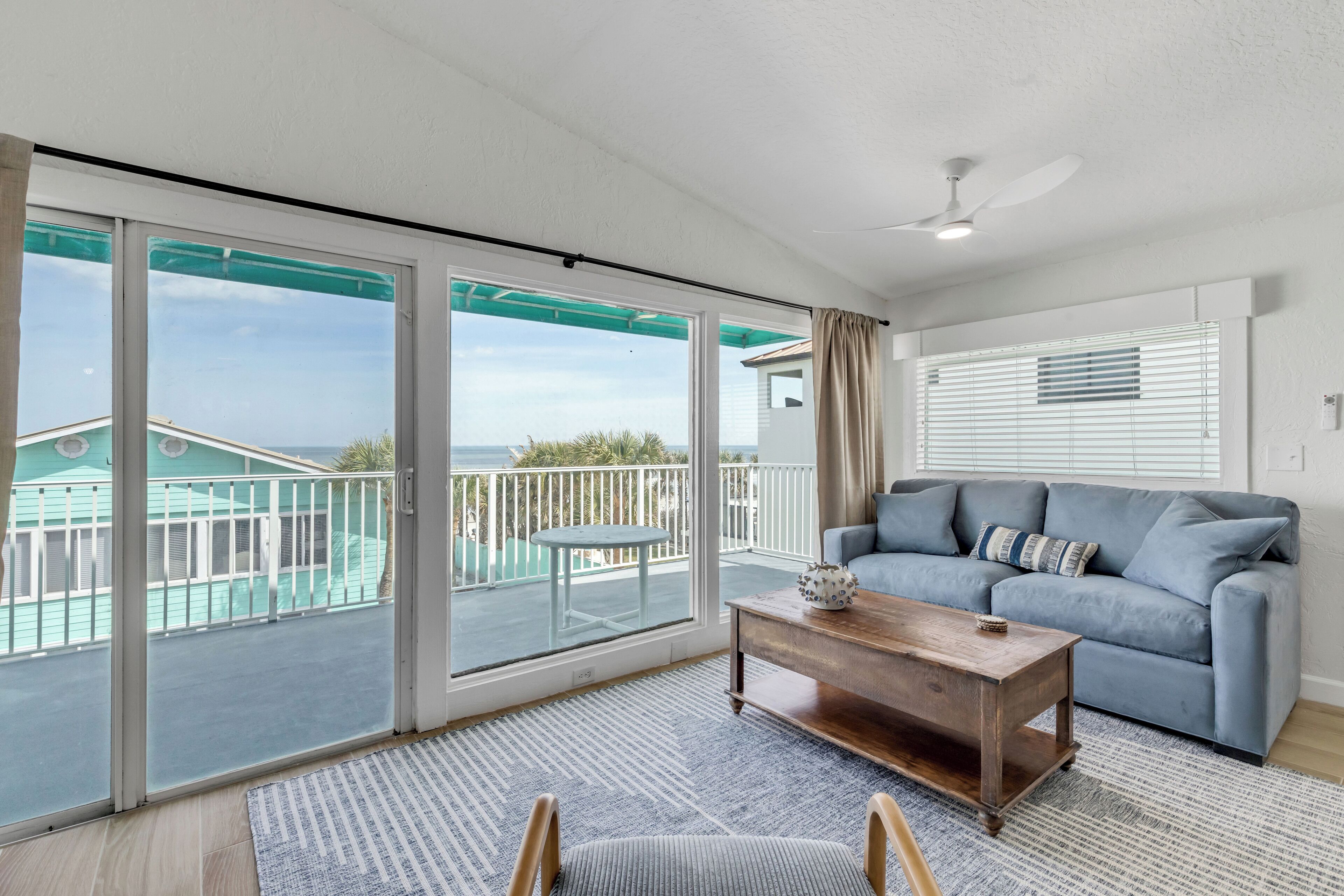 Un'ampia stanza con un balcone, un divano blu, un tavolino in legno e vista sul mare.