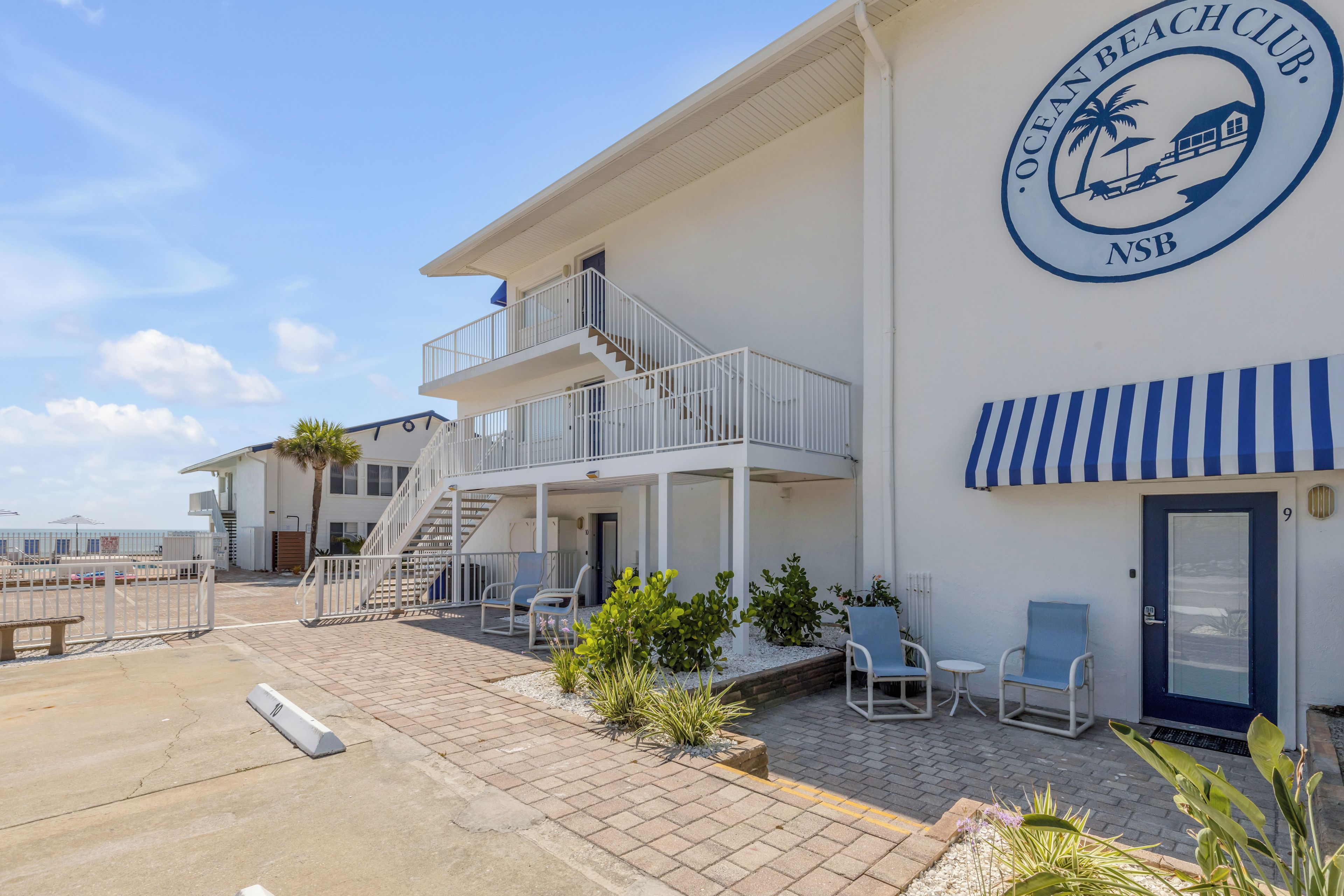Une propriété située en bord de mer, comprenant un bâtiment à deux étages, un patio couvert avec des sièges et une vue dégagée sur l’océan.