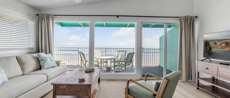 A living room with a sofa, coffee table, and chair, a television, and a balcony with a view.