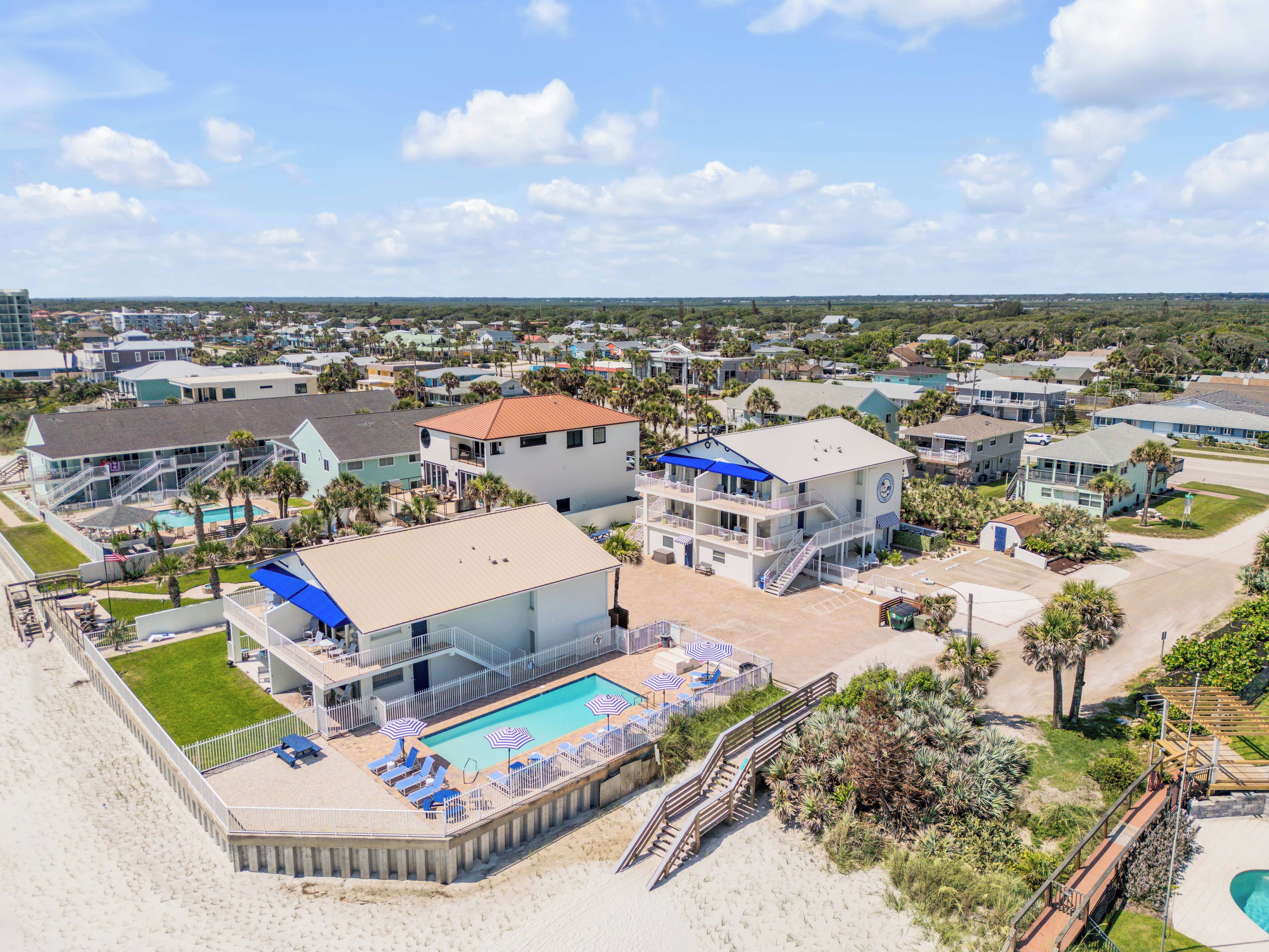 A beachfront hotel with a swimming pool, multiple balconies, and a beach area with sun loungers.