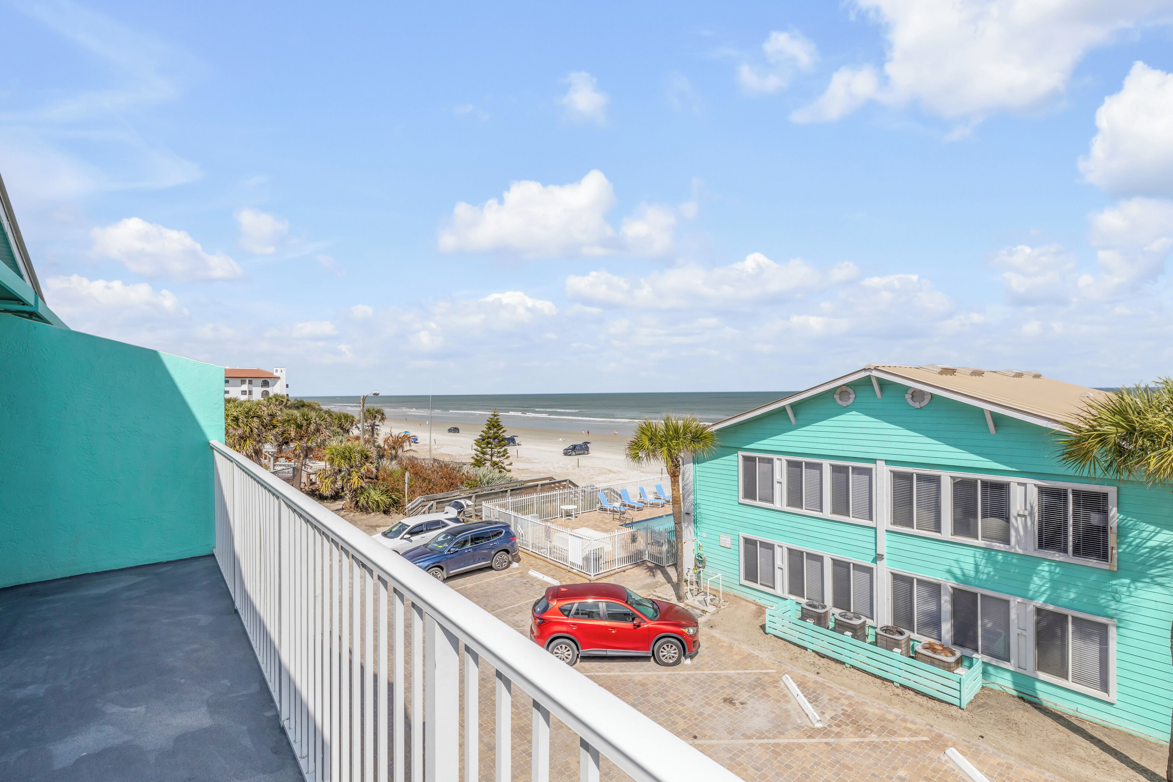 Un edificio turquesa con un balcón que da a una playa.
