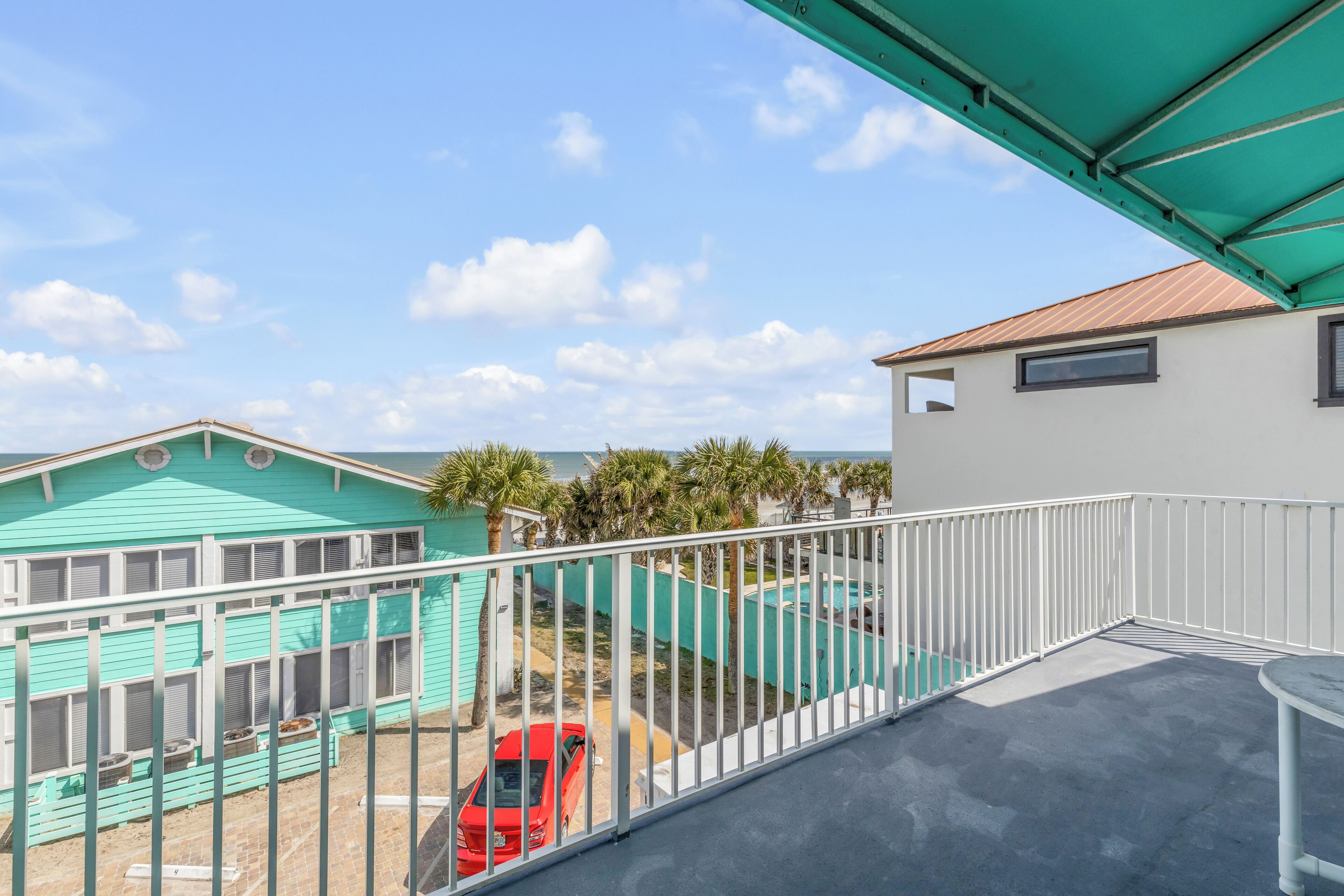 A balcony with a view of a turquoise building and a red car parked outside.