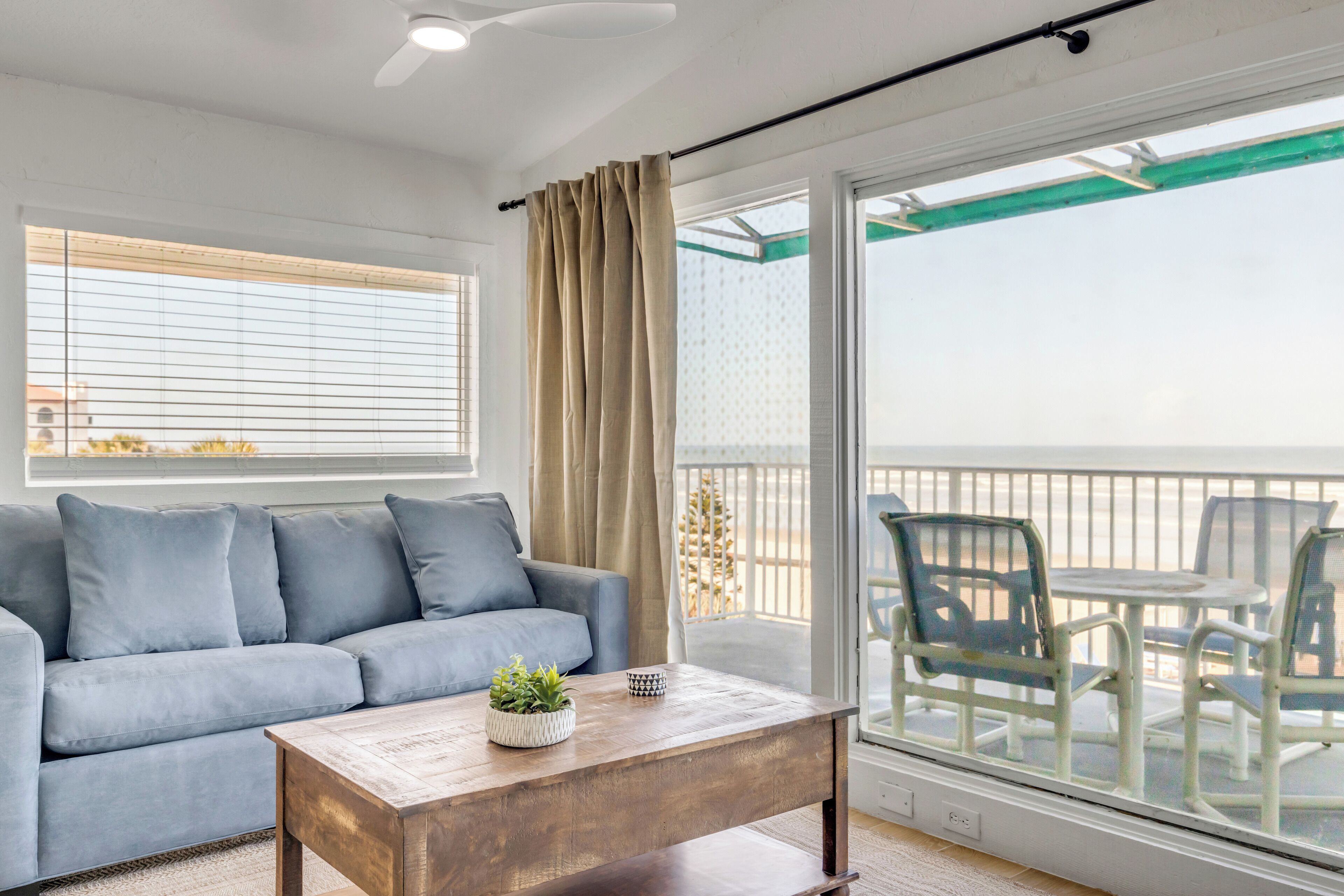 Un balcon avec vue sur la mer, un canapé gris et une table basse en bois agrémentée d’une plante.