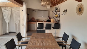 A dining area with a wooden table and black chairs, a kitchen in the background, and a ceiling with wooden beams.