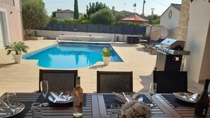 A poolside dining area with a table set for two, a bottle of wine, and a bouquet of flowers.