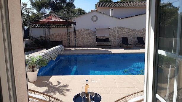 A swimming pool with lounge chairs and a table with a bottle and glass.