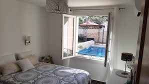 A bedroom with a large bed, a window with a view of a swimming pool, and a ceiling fan.