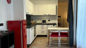 A compact kitchen with white cabinets, a red refrigerator, and a dining area with a table and chairs.