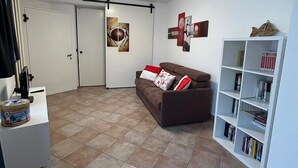 A living room with a brown sofa, a white bookshelf, and a door leading to another room.