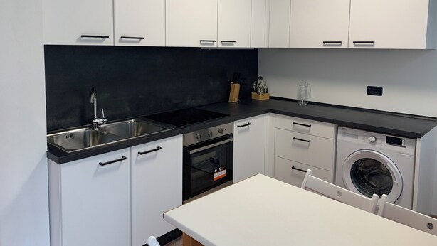 A modern kitchen with white cabinets, a black countertop, stainless steel sink, and built-in appliances including a dishwasher and washing machine.