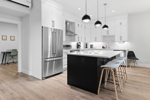 Une cuisine moderne dotée d’appareils électroménagers en acier inoxydable, d’un grand îlot central et de tabourets de bar.