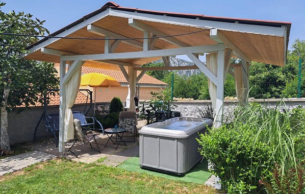 A covered outdoor patio with a hot tub, seating area, and a pergola structure.