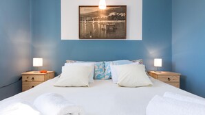 Une chambre à coucher avec un lit, deux tables de chevet et un tableau représentant un paysage côtier accroché au mur.