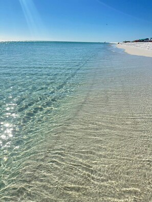 A beach with clear shallow waters and a sandy shore.