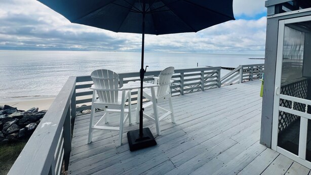 A wooden deck with a view of the ocean, a white chair, and a large umbrella.