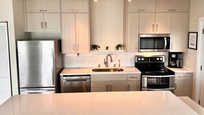 A modern kitchen with stainless steel appliances, light-colored cabinets, and a marble countertop.